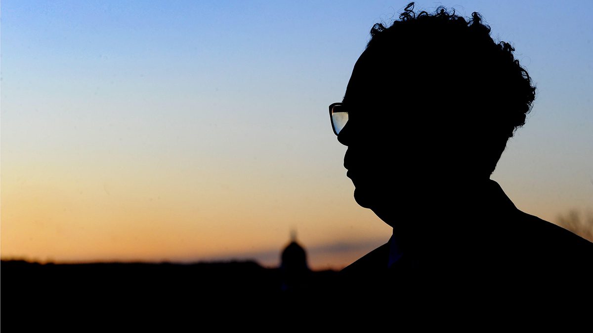 A silhouette image of Justin Andrus, posing for a photo with the dome of the Maine State House in the distant background.
