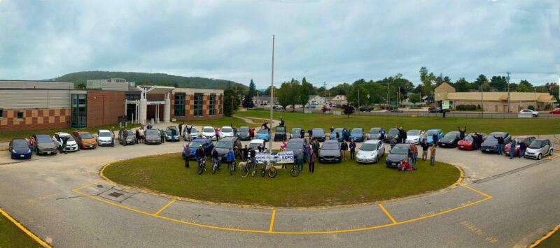 A panorama photo of people posing next to electric vehicles.