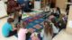 Teacher Cristina Perez Zamora sits at the head of a half circle of students sitting on a carpet in a classroom during a lesson.