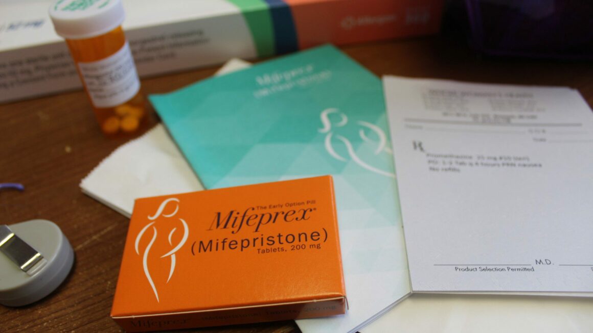 An orange box of the mifepristone abortion pill sits on a table among booklets and a pill bottle.