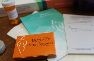 An orange box of the mifepristone abortion pill sits on a table among booklets and a pill bottle.