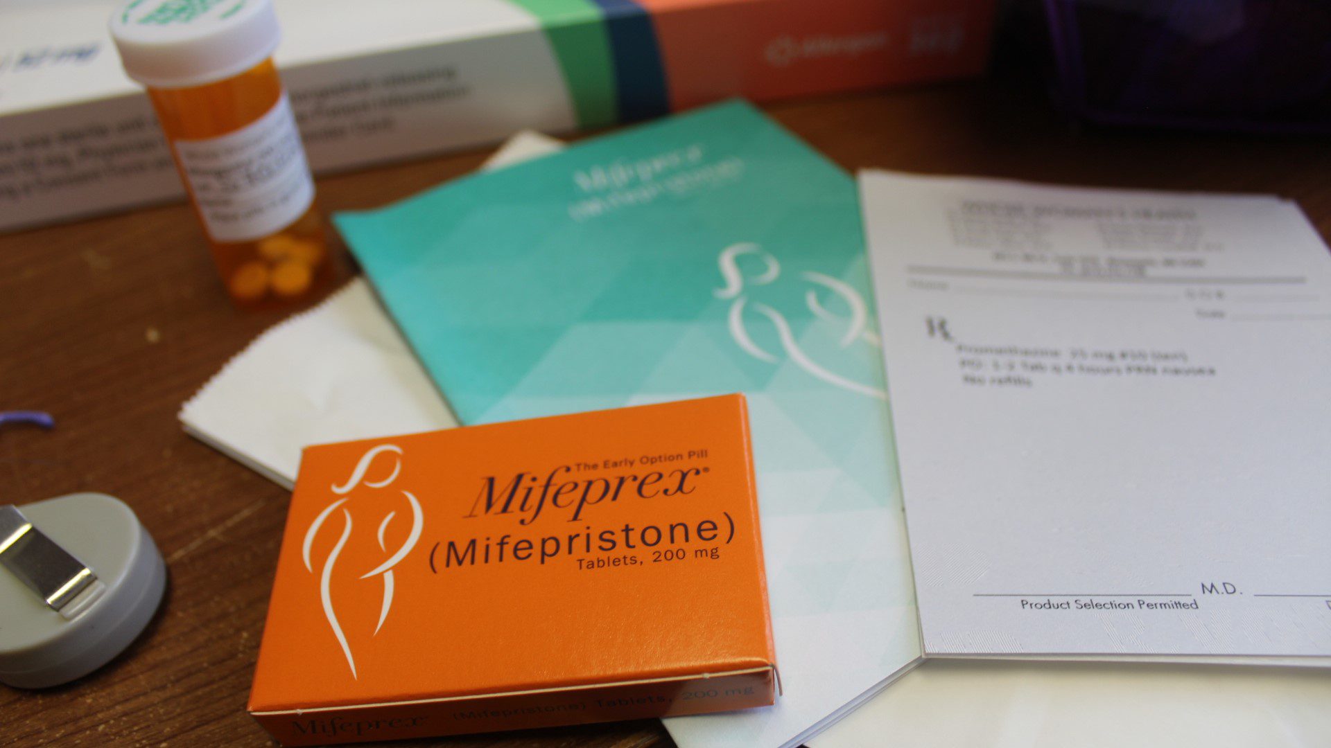 An orange box of the mifepristone abortion pill sits on a table among booklets and a pill bottle.