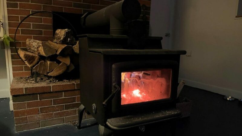 A wood stove, in use, in front of a fireplace.