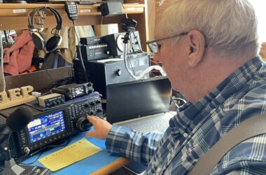 Phil Duggan sits at his desk while operating ham radio controls.