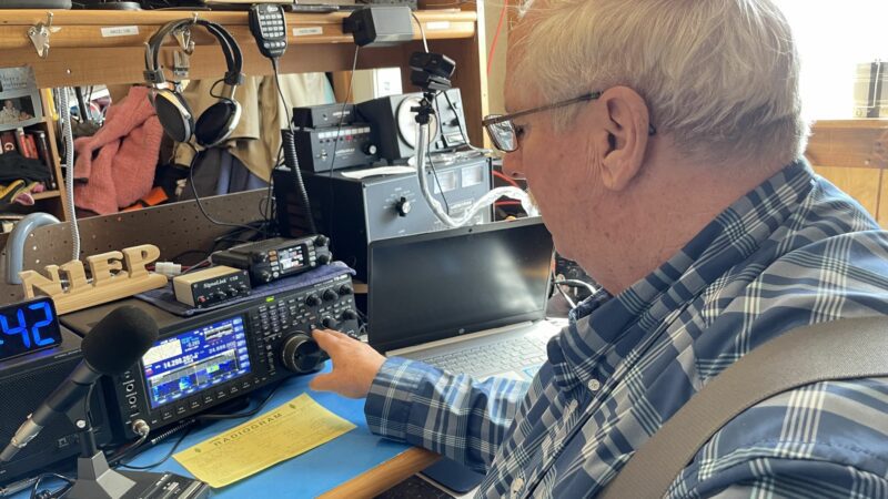 Phil Duggan sits at his desk while operating ham radio controls.