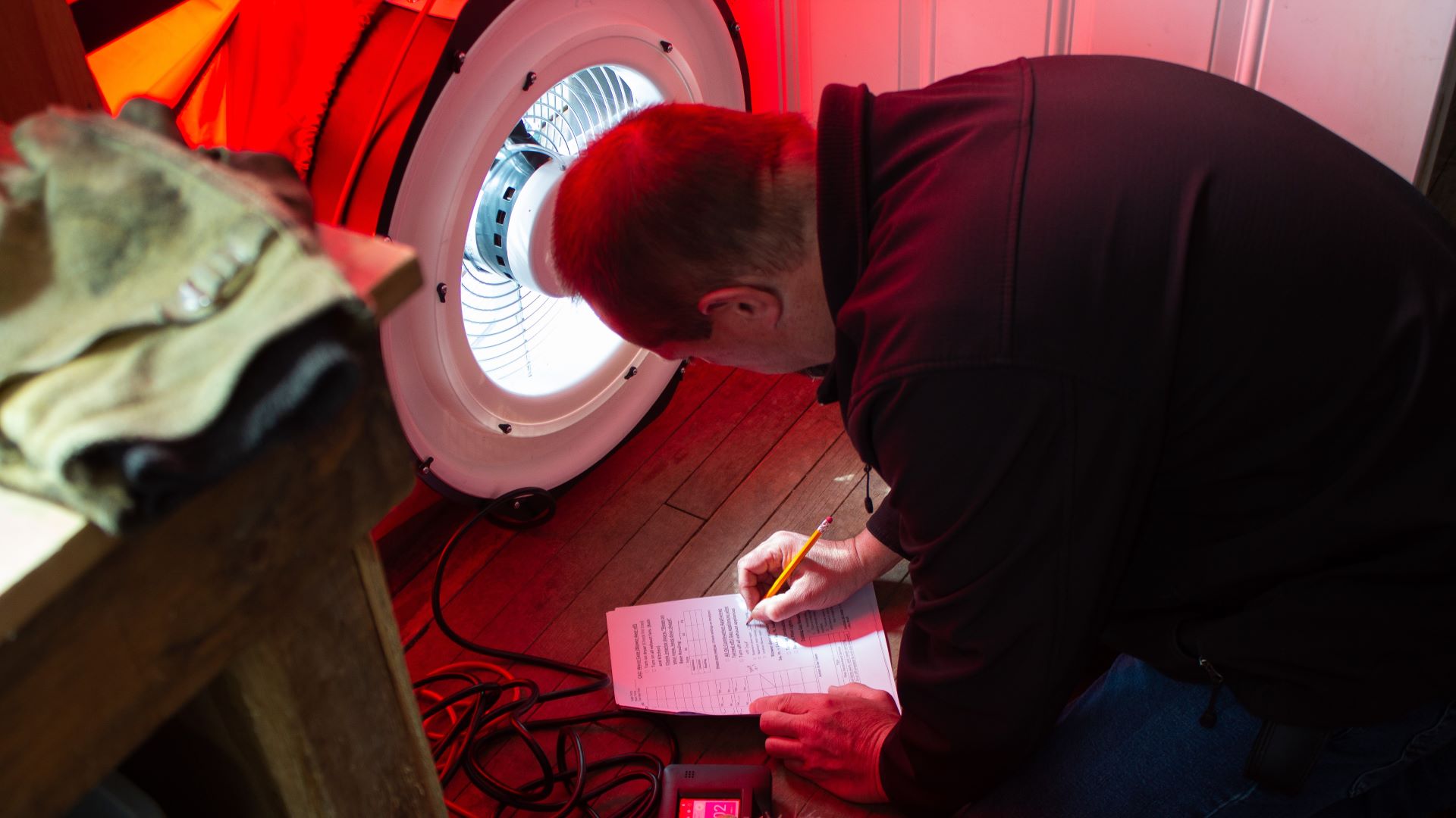 A man takes notes while performing a blower door test in a residence. 