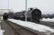 Black rail cars sit in a railyard.