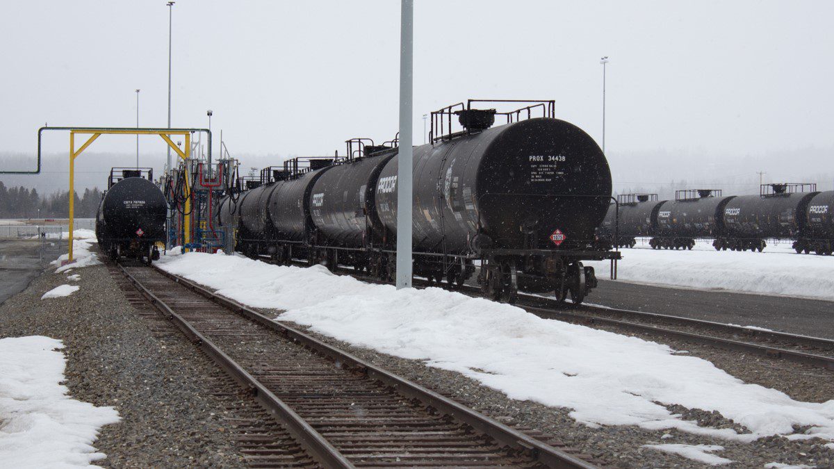 Black rail cars sit in a railyard.