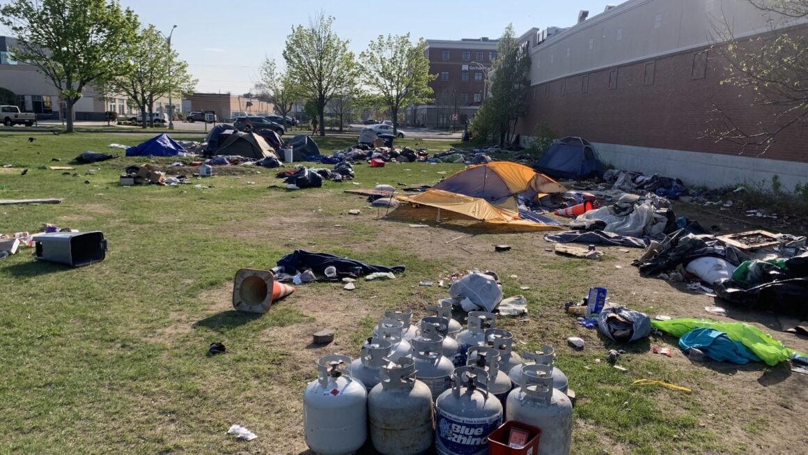 Tents, trash and a pile of propane tanks are seen around the grassy homeless campsite at Bayside.