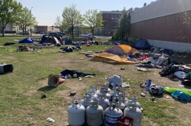 Tents, trash and a pile of propane tanks are seen around the grassy homeless campsite at Bayside.