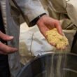Yellow sawdust fills and spills out of a hand that is hovering over a garbage can.