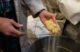 Yellow sawdust fills and spills out of a hand that is hovering over a garbage can.