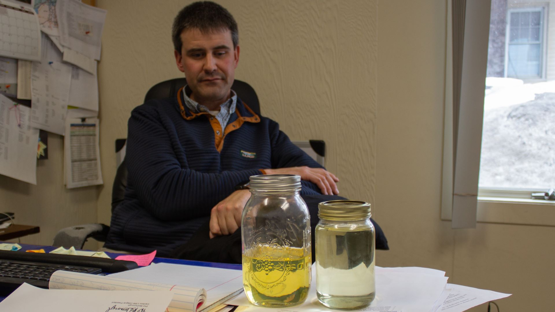 Ryan Rogers sits at his desk with jars wood- and plant-based biofuels sitting on the desk.