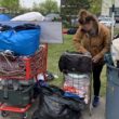 A woman gathers her belongings using shopping carts and a trash can.