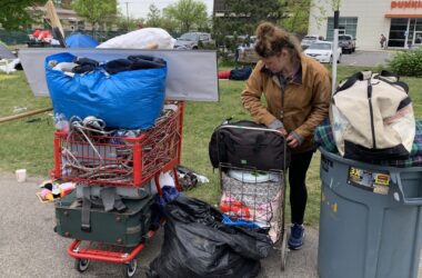 A woman gathers her belongings using shopping carts and a trash can.