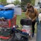 A woman gathers her belongings using shopping carts and a trash can.