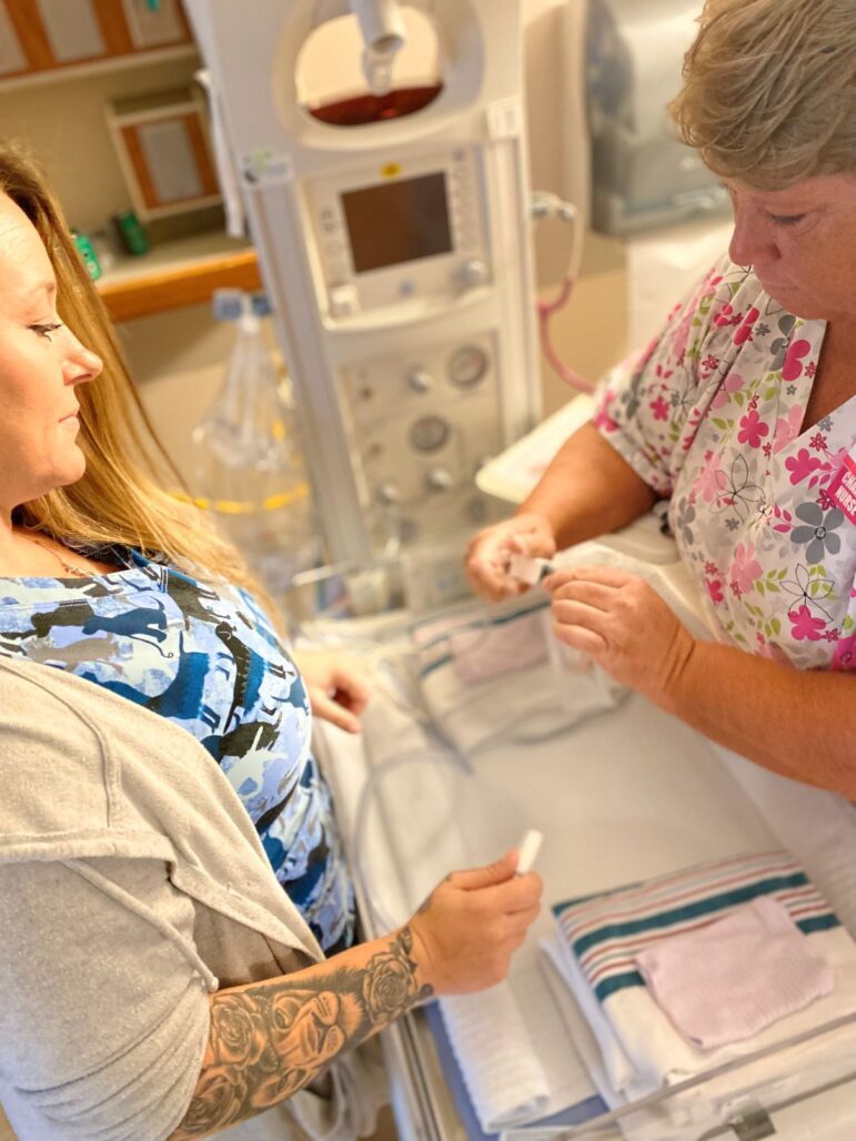 Two nurses demonstrate how to use a piece of equipment to check a newborn's vital signs.