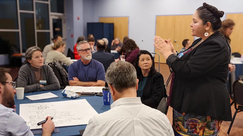 Danae Wilson stands while speaking to a table of five individuals.