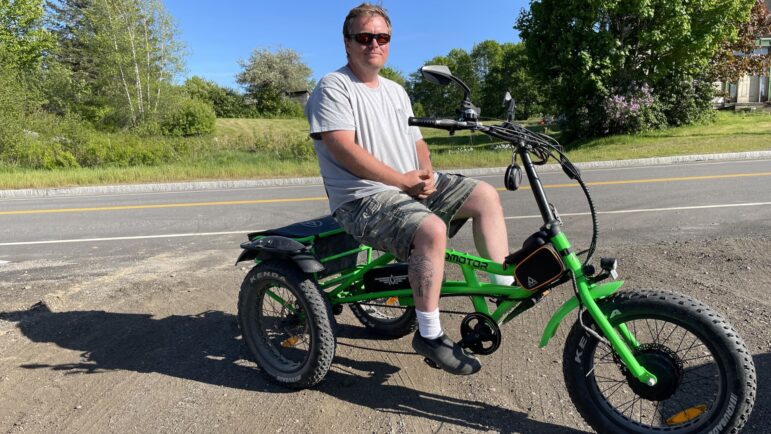 David Ginn poses for a photo while sitting on his large green bike.