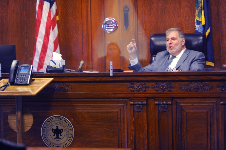 Judge Paul Aranson motions with his right hand while sitting at his desk in a courtroom.