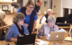 An instructor looks over the shoulders of two women sitting in front of laptops.
