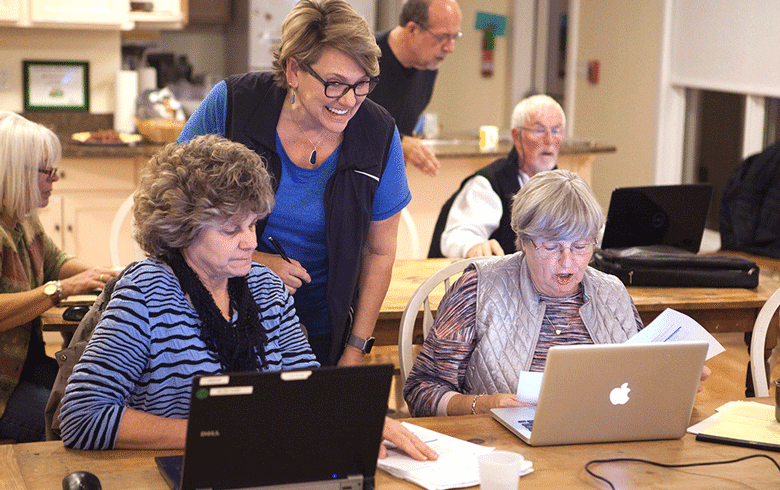 An instructor looks over the shoulders of two women sitting in front of laptops.