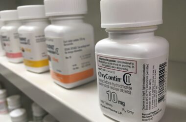 A white bottle of oxycodone sits on a shelf among other white pill bottles.