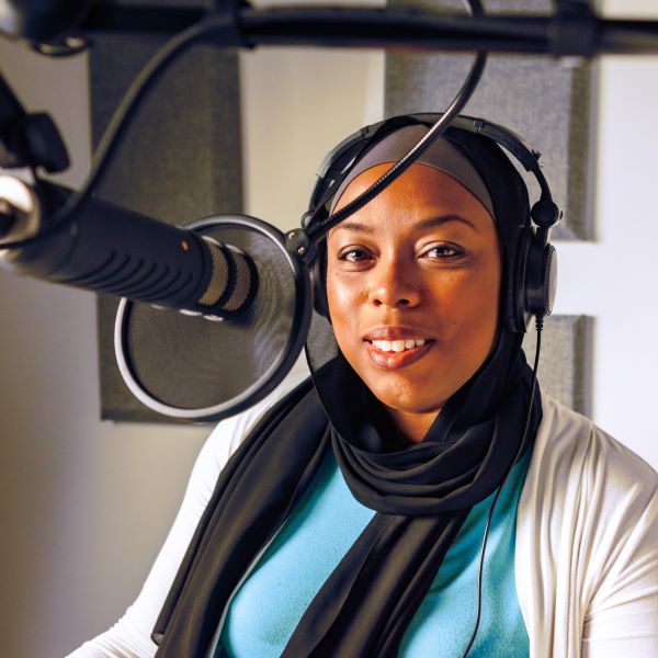 Adilah Muhammed sits in front of a podcast microphone.