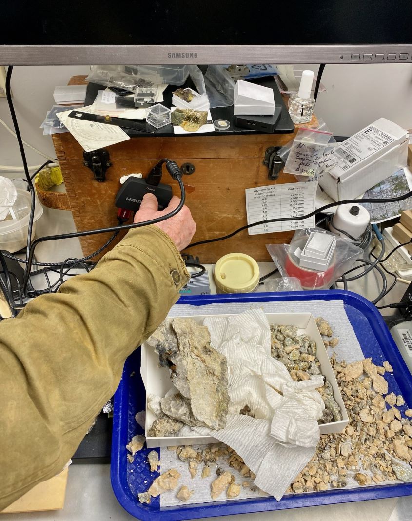 The hand of Al Falster controls a monitor input while the surface area of the lab is cluttered.