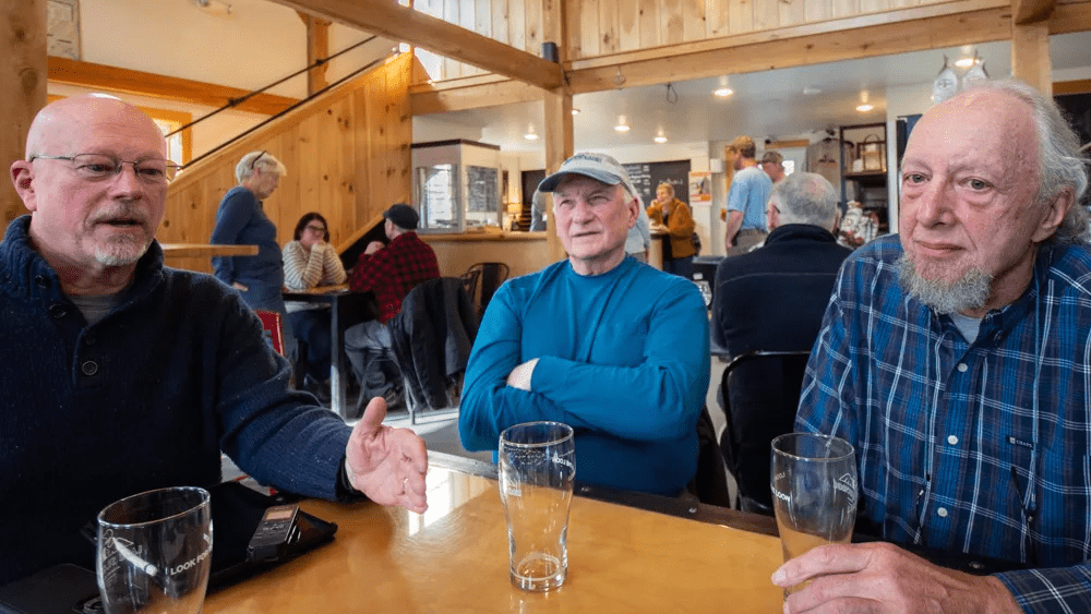Three men sitting around a table in a restaurant chatting during an interview.