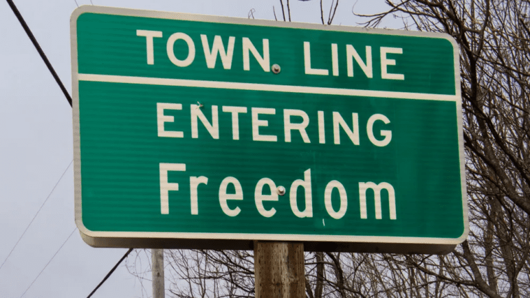 A green road side that reads "Town Line. Entering Freedom."