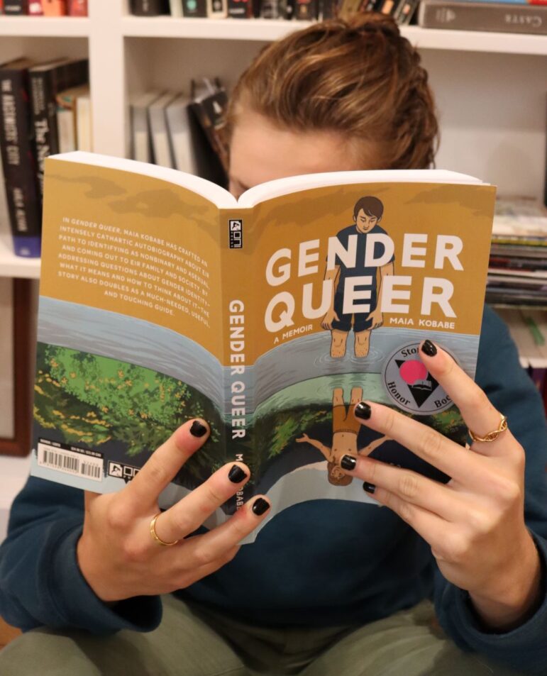 An individual reads the book Gender Queer. 