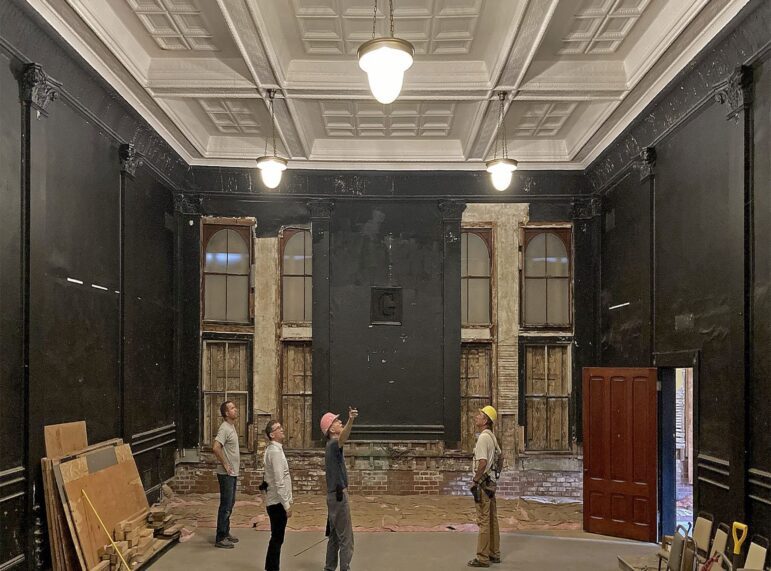 Four construction workers look toward the ceiling inside the Masonic Hall.