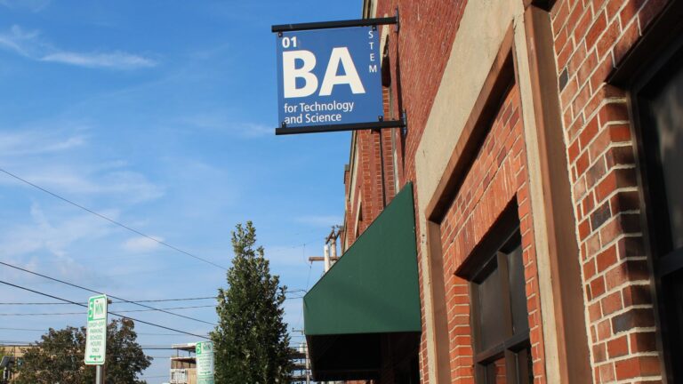 A blue sign hanging from a brick wall for Baxter Academy.