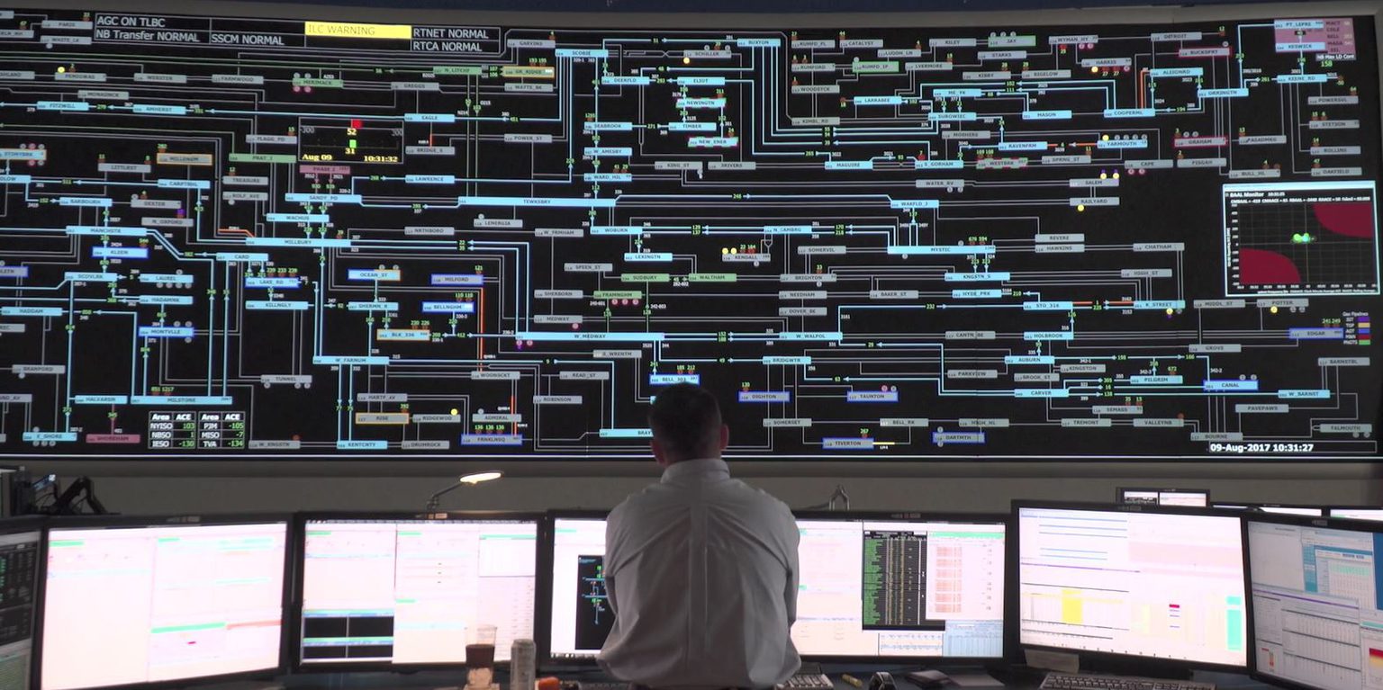 An inside look at the control room of ISO-NE. A man is looking at numerous monitor displays in the control room.