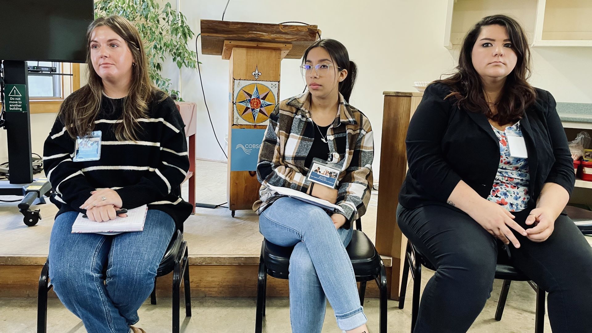 Three female panelists sit in chairs on stage.