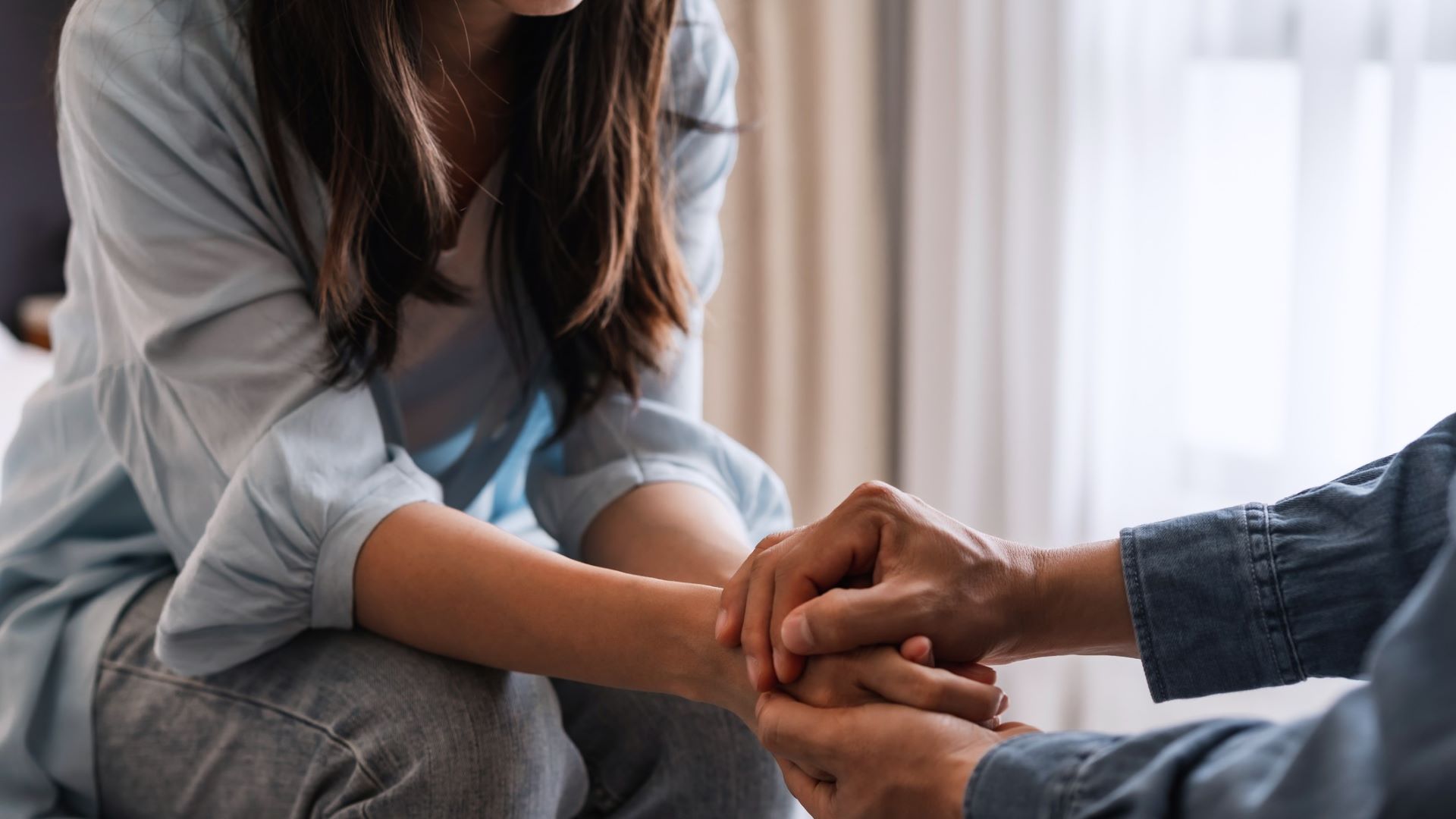 Two individuals hold each other's hands in a sign of comforting the other in this stock image.
