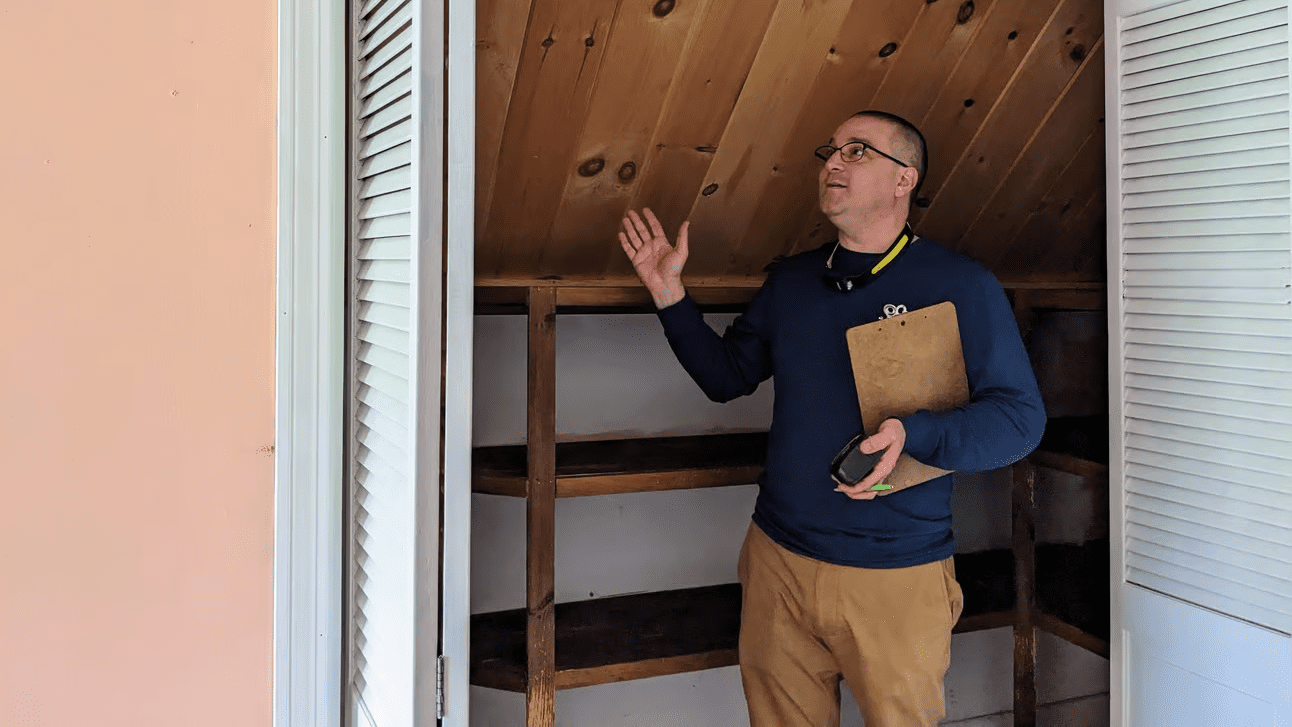 An energy auditor standing in a closet while looking up and gesturing with his right hand.