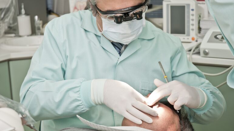 A dentist uses a headlamp to examine the inside of a patient's mouth.