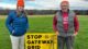 Holly Noyes and Chuck Noyes pose for a photo next to a yellow stop gateway grid yard sign.