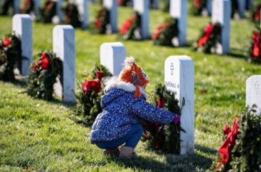 A young girl places a wreath against a headstone.