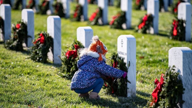 A young girl places a wreath against a headstone.