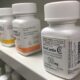 A white bottle of oxycodone sits on a shelf among other white pill bottles.