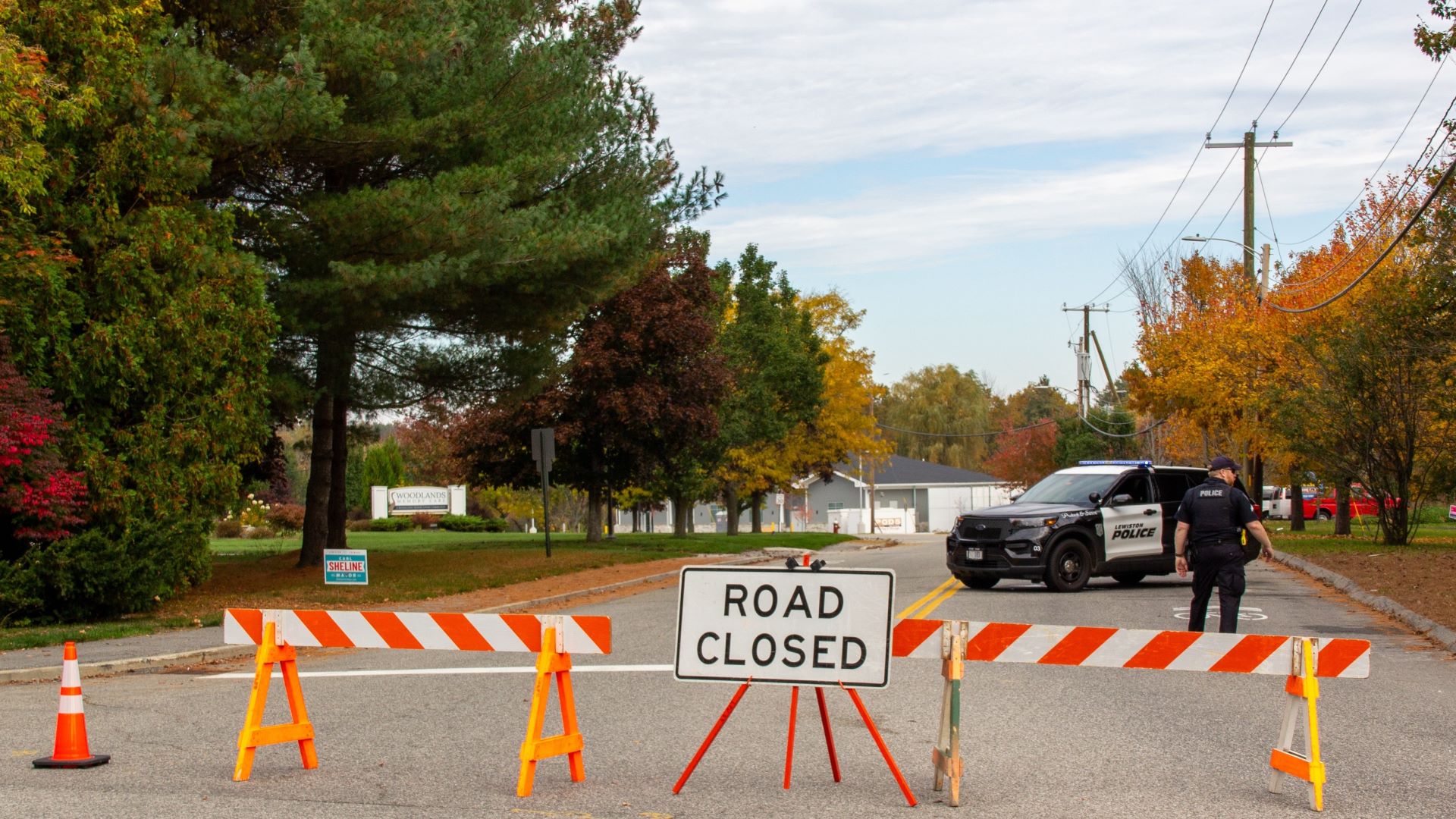 A police cruiser and police officer seen past a road closure barrier.