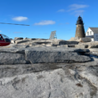 A red helicopter on the rocks by a lighthouse.