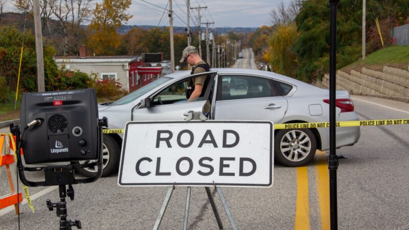 A police officer stands next to an unmarked vehicle.