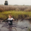 A young woman playing in a muddy marsh.