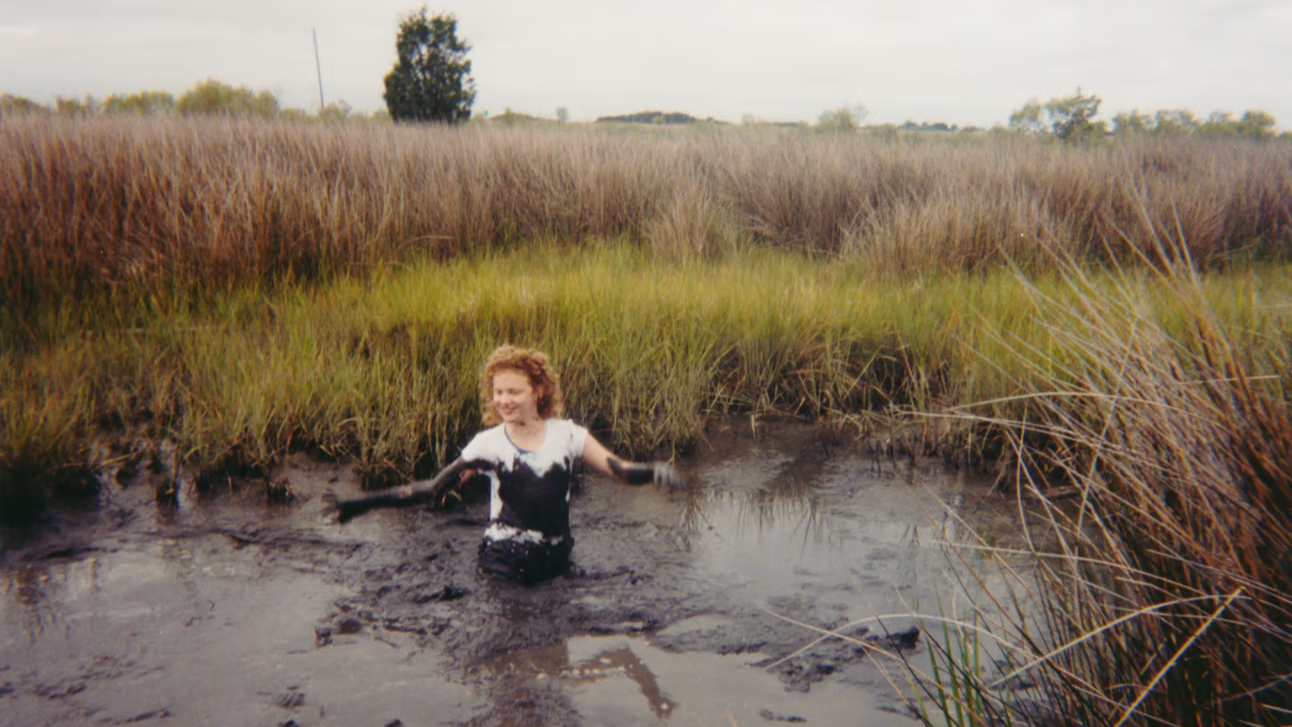 A young woman playing in a muddy marsh.