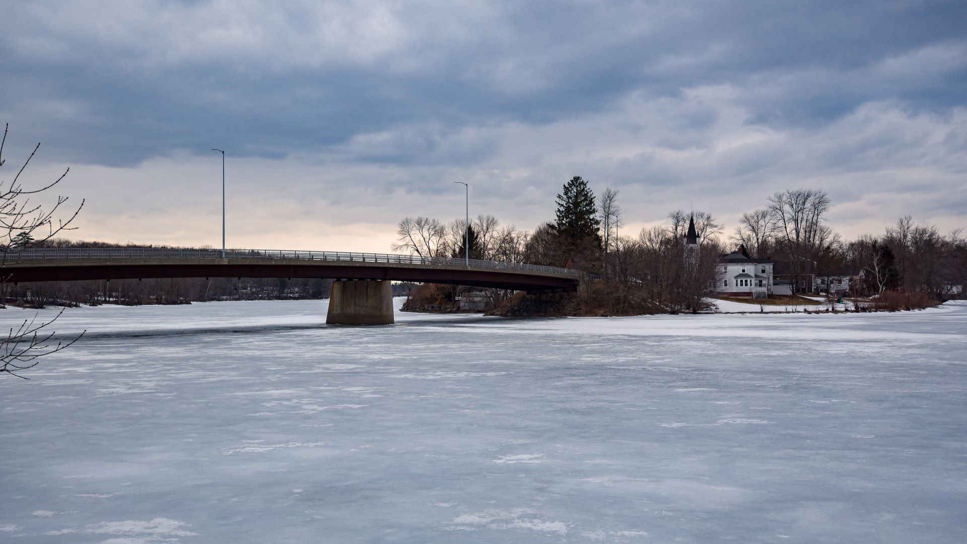 A bridge hovers over a frozen body of water.