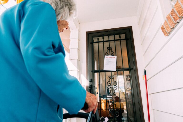 An elderly woman looks at an eviction notice on her door.